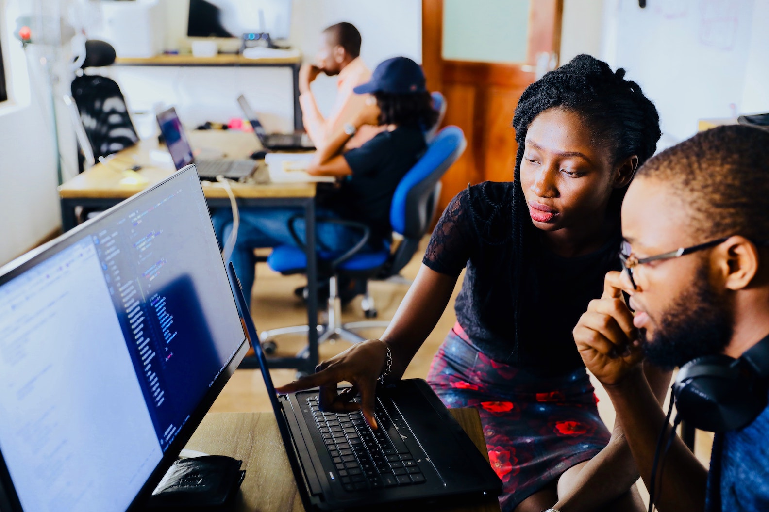 A Black woman with braids and a Black man with a beard and glasses work together on the computer