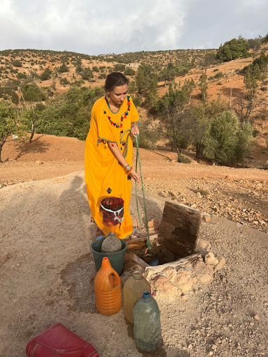 Photo of a person in a yellow dress drawing water from a well