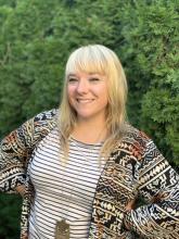 A head-and-torso picture of a woman with shoulder-length blond hair. She is wearing a patterned shirt and sweater and is smiling.