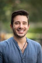 A head-and-shoulders picture of a man with short dark hair. He has a blue shirt and is smiling.