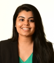 A head-and-shoulders picture of a woman with long brown hair. She is wearing a green shirt and black blazer, and is smiling