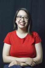 A head-and-shoulders picture of a woman with shoulder-length dark hair. She is wearing a red shirt and is smiling.