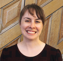 light skinned woman with brown haired bangs, black shirt in front of wood paneling