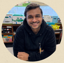 smiling brown skinned man with black hair and navy sweatshirt in front of bookshelf