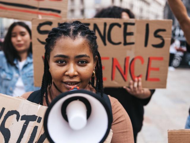 Students protesting, led by a Black woman with braids carrying a megaphone