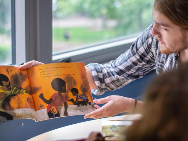 A man reads a picture book to a student.
