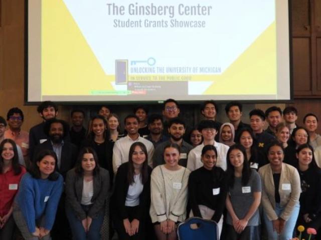 A group of students standing in front of a projector screen with the words The Ginsberg Center Student Grants Showcase.