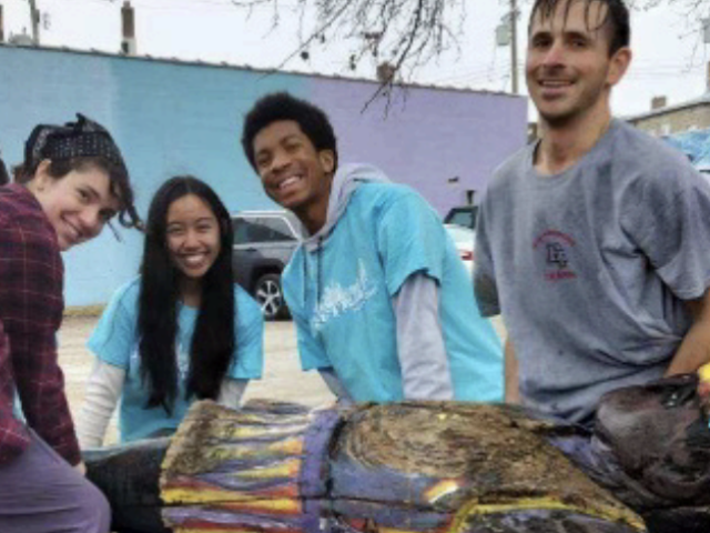 Four student stand behind a piece of art.