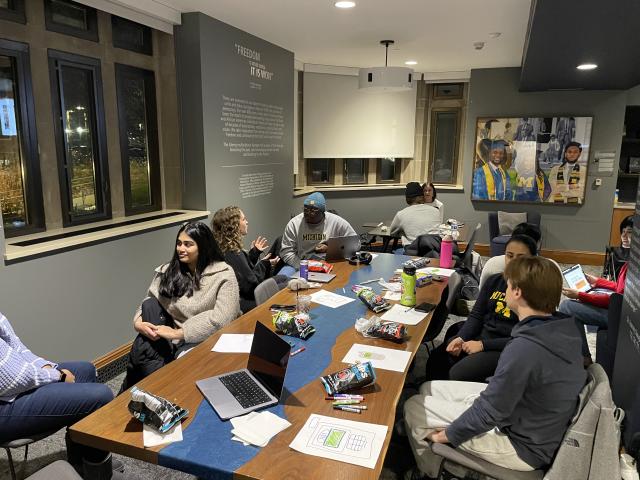 A group of students seated at a table talking in pairs.