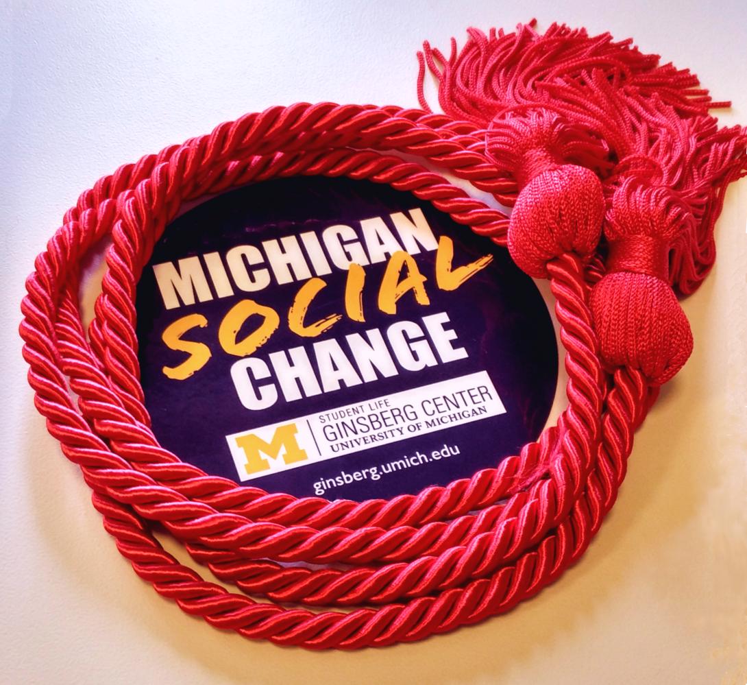 a picture of red braided graduation cords in a circle, ringing a sticker with the words Michigan Social Change on it